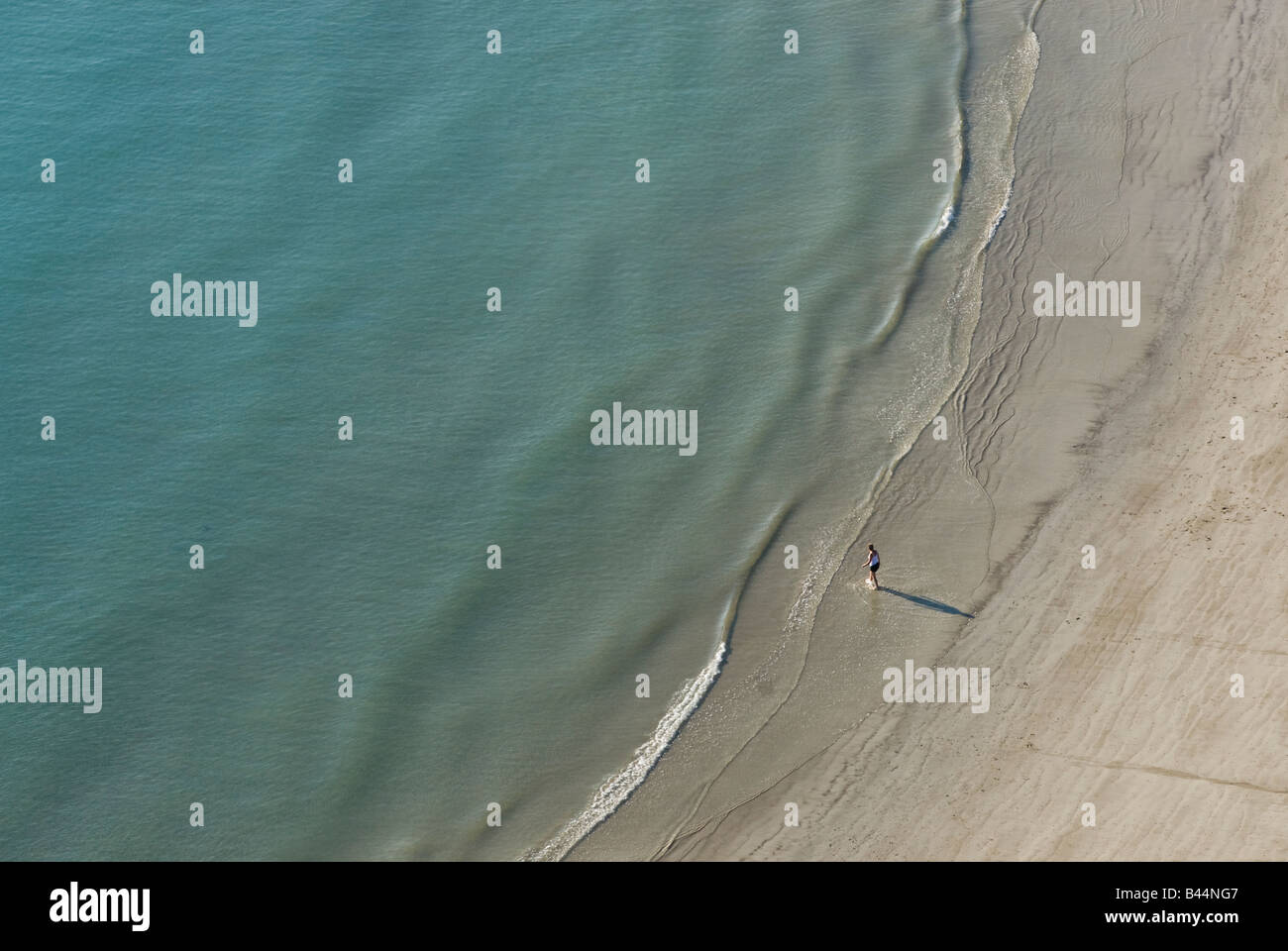 Luftaufnahme der Person stand allein am Rand des Wassers am Sandstrand Stockfoto