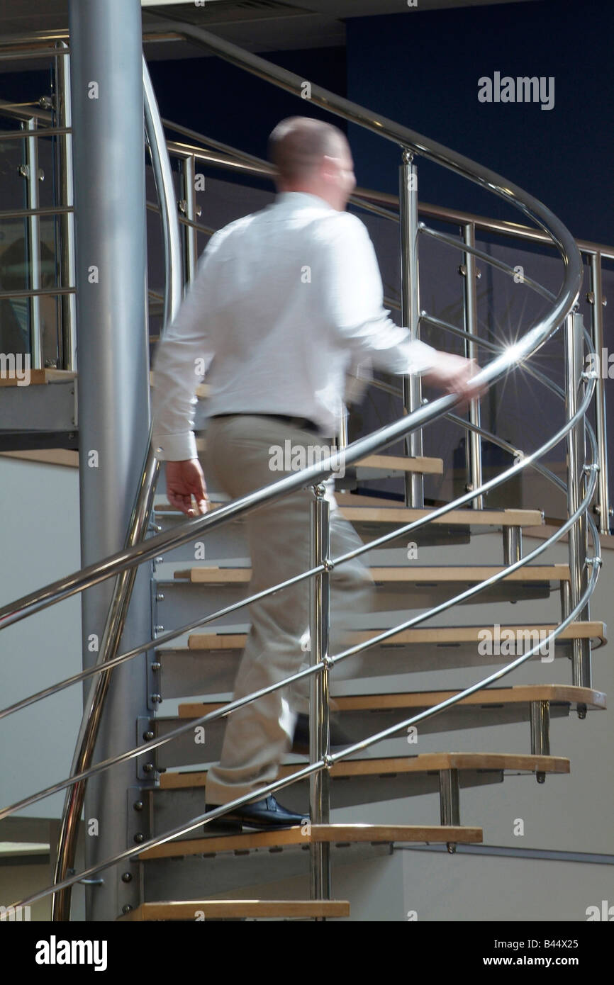 Mann Klettern eine Edelstahl Wendeltreppe in ein modernes Großraumbüro Stockfoto