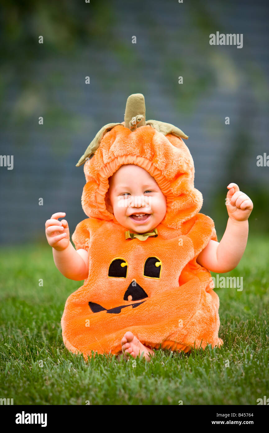 Baby in einem Kürbis Halloweenkostüm sitzen auf Rasen Stockfoto