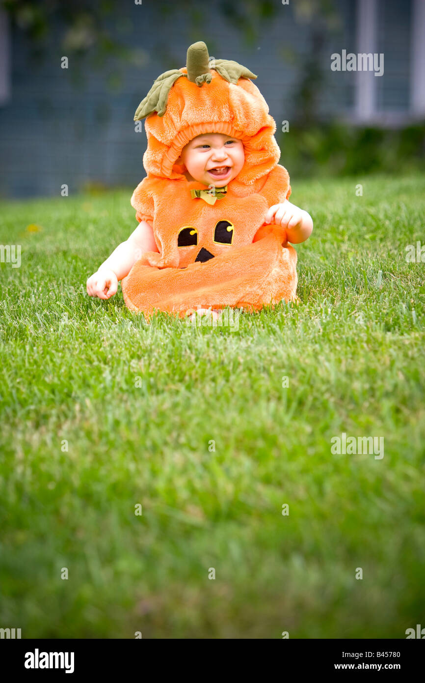 Baby in einem Kürbis Halloweenkostüm sitzen auf Rasen Stockfoto