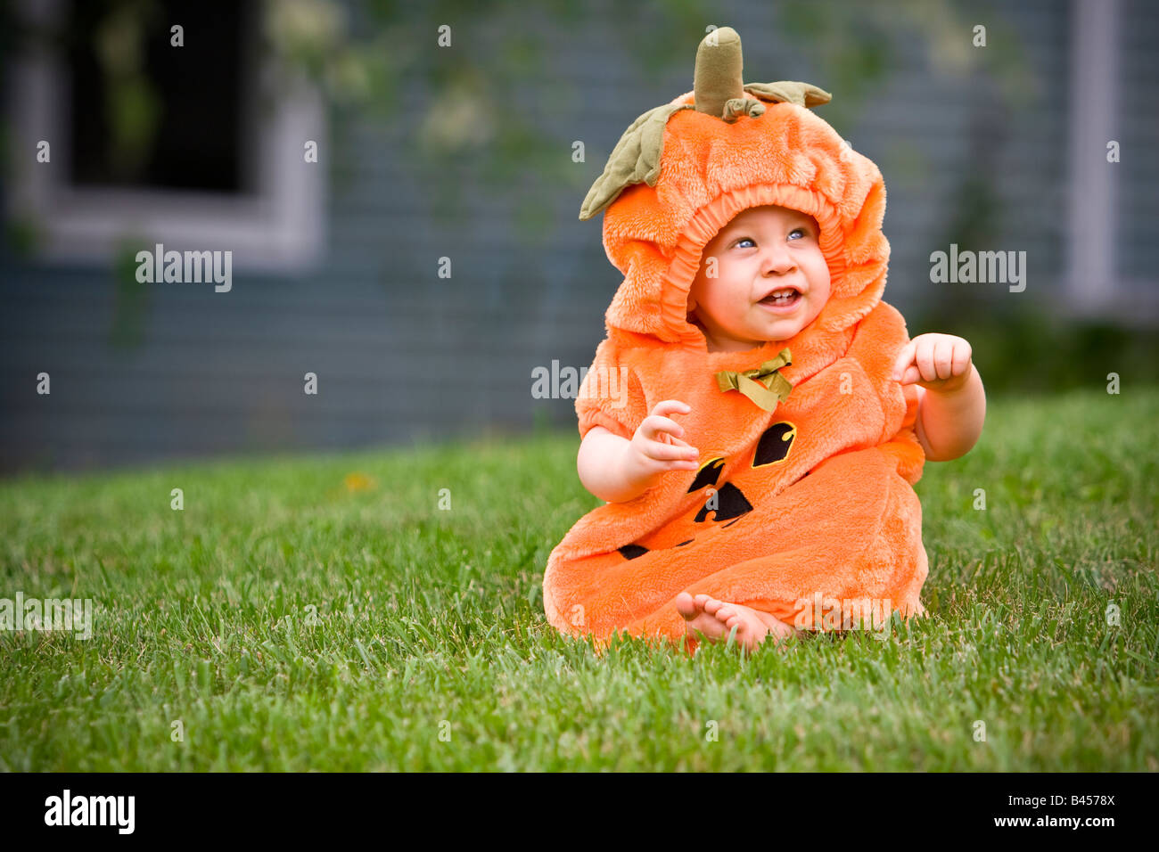 Baby in einem Kürbis Halloweenkostüm sitzen auf Rasen Stockfoto