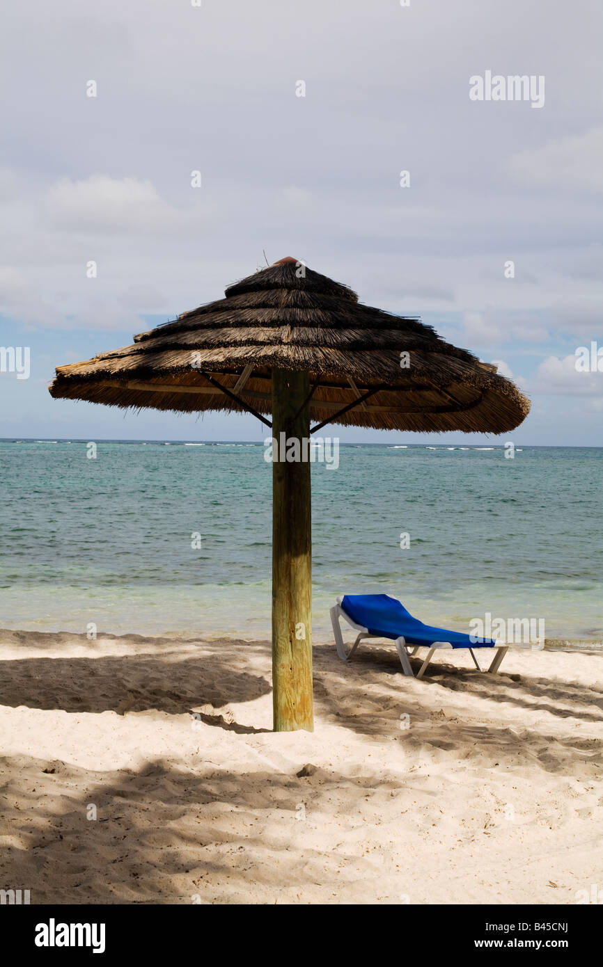 Ein blaues Bett und Stroh Sonnenschirm für Schatten am Strand auf der karibischen Insel Antigua Stockfoto
