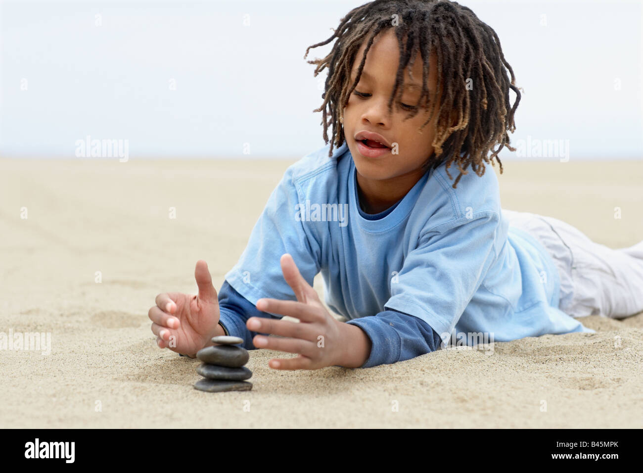 Gemischte Rennen junge Stapeln Steinen auf sand Stockfoto