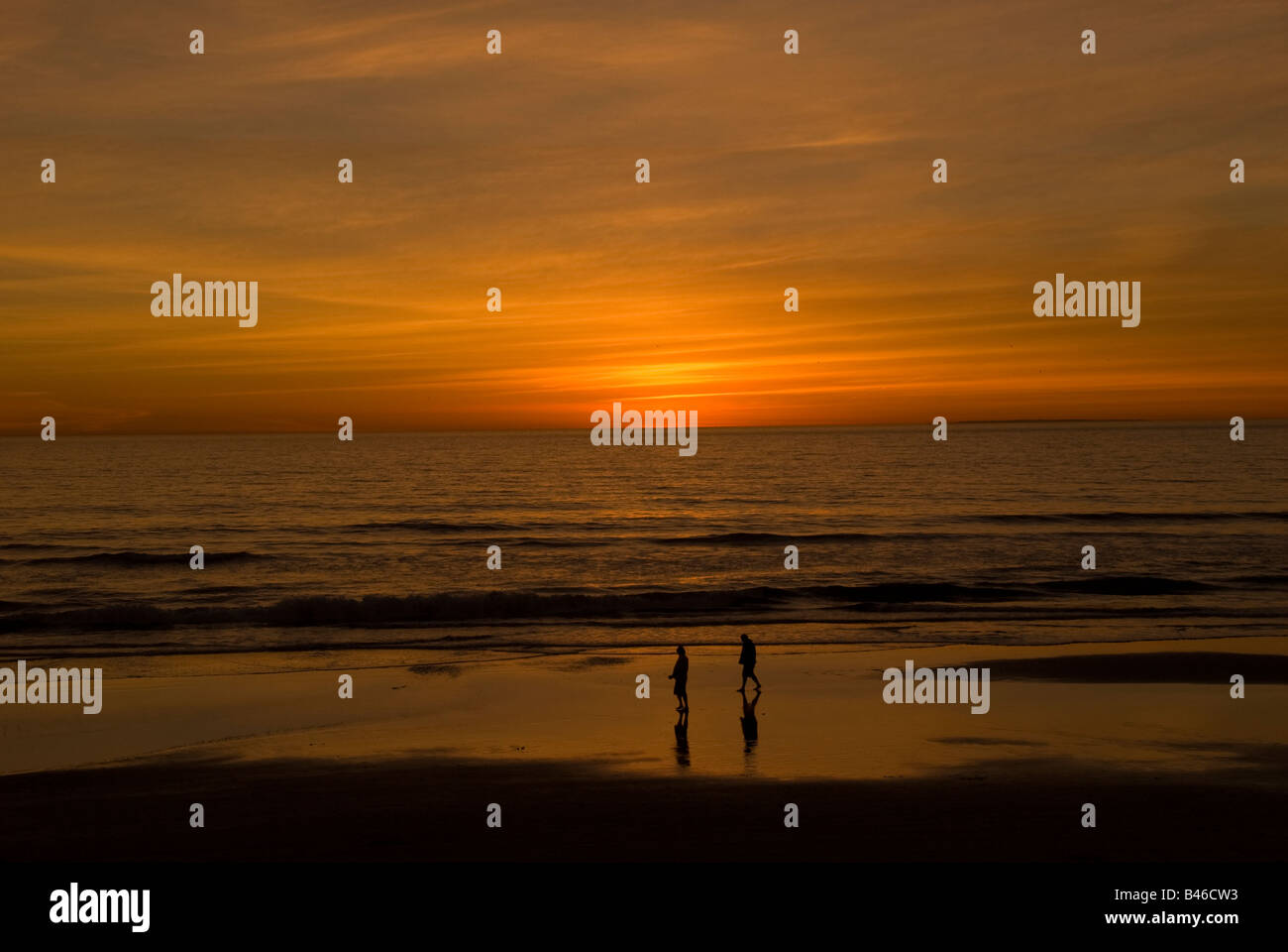 Zwei Menschen, die zu Fuß entlang der Kante des Wassers kurz nach Sonnenuntergang auf Oceanside Beach Kalifornien Stockfoto