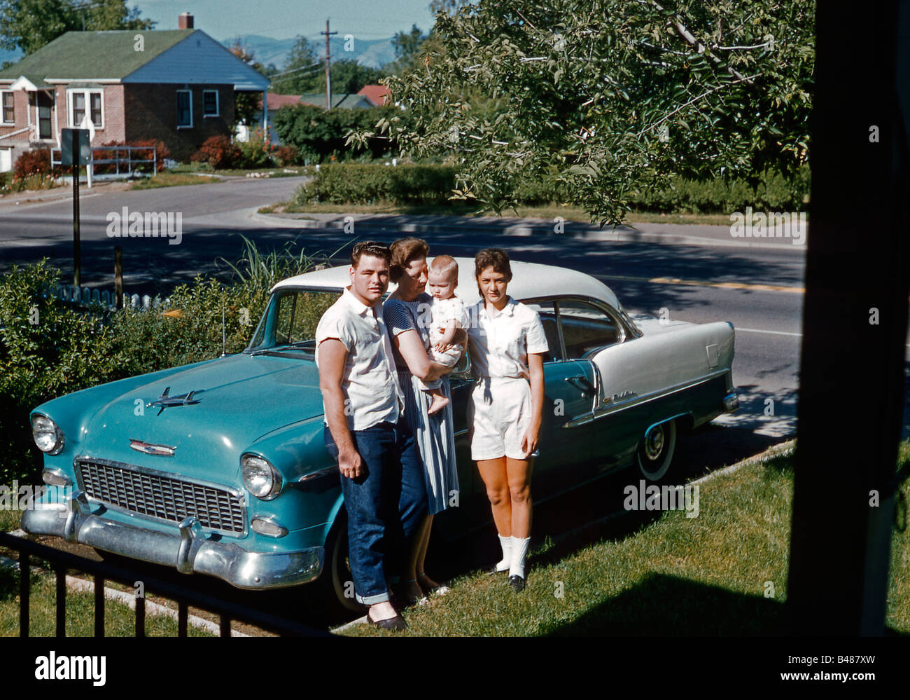 Eine Familie posiert neben ihrem Chevrolet Bel Air in ihrer Vorstadteinfahrt, USA, 1961 geparkt. Die Gruppe umfasst das Baby des jungen Paares. Stockfoto