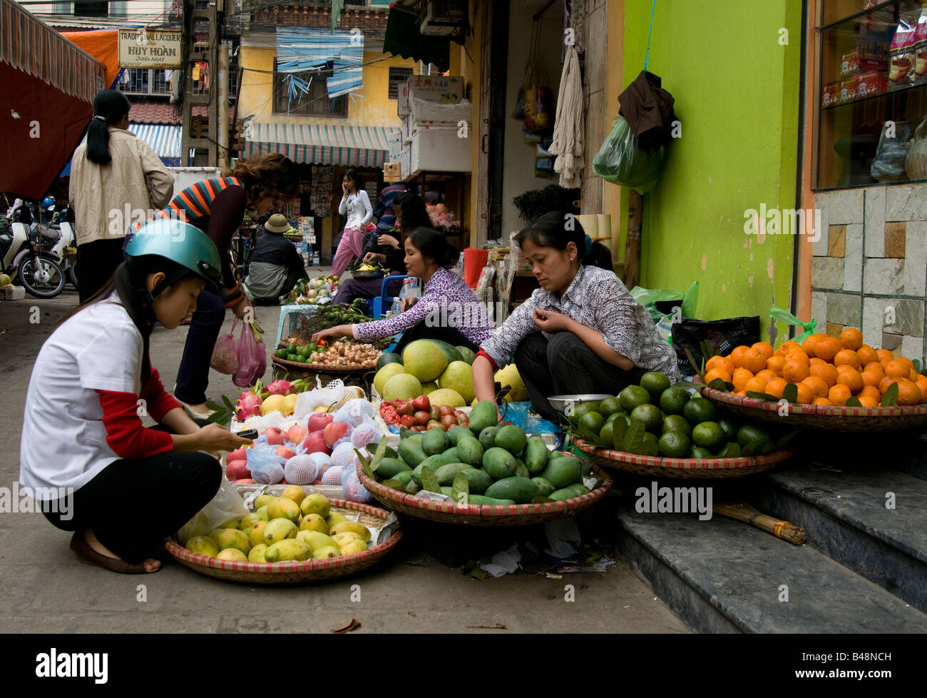 Eine Frau kniet an ein frisches Obst stand auf den Stufen des einen Shop Eingang in einen Straßenmarkt Hanoi Vietnam eingerichtet Stockfoto