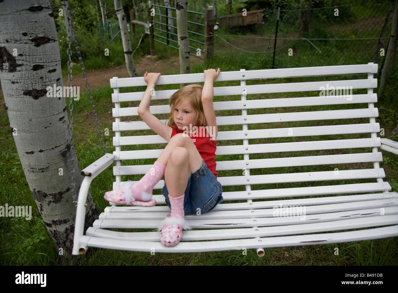 Ein junges Mädchen ruht auf einer weißen Bank Schaukel und spielt auf Schaukel auf der grünen Wiese bei einem Familienurlaub in der utah Stockfoto