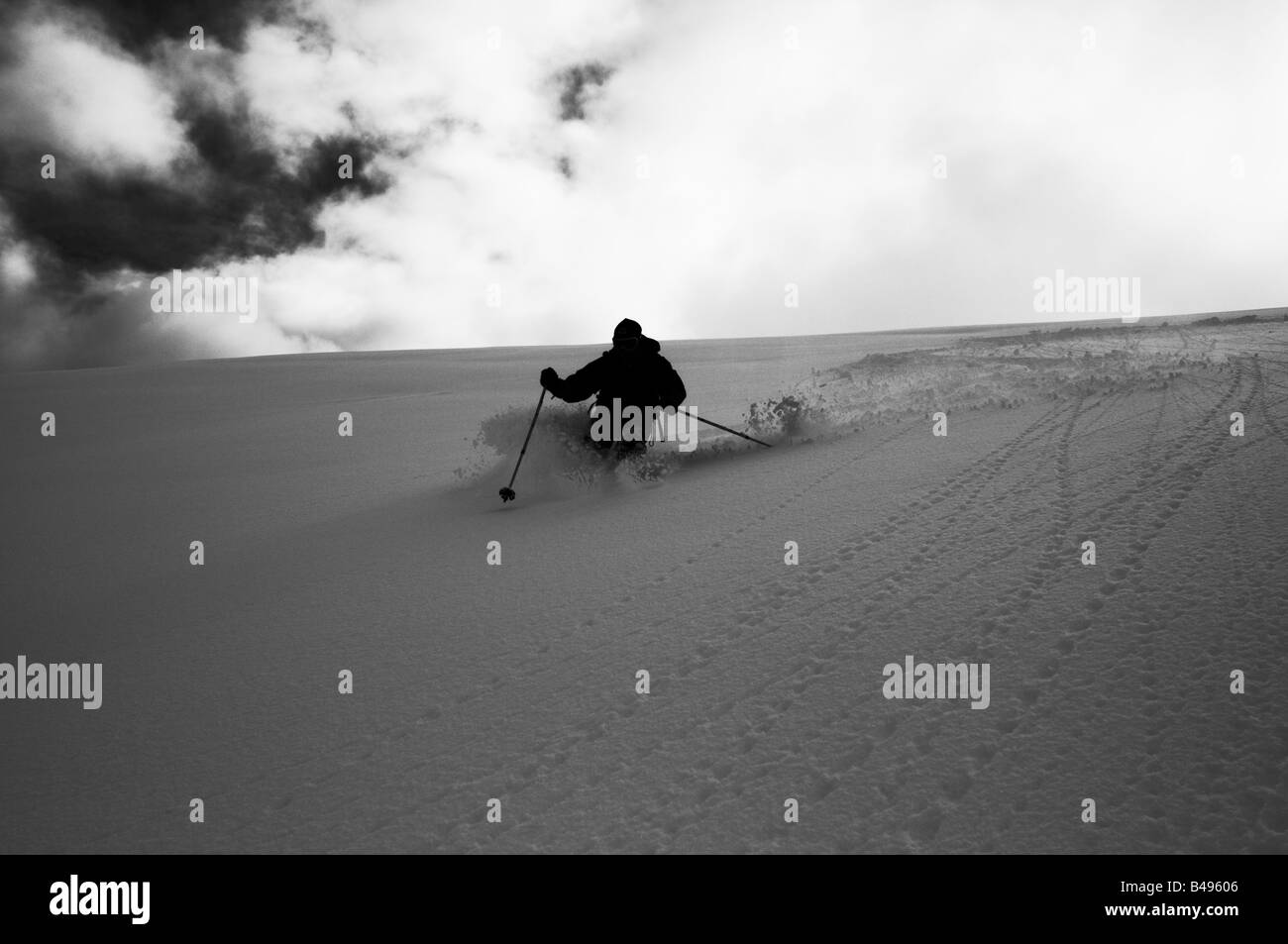 Ein Skifahrer absteigend unberührten Hang und Silhouette gegen ein bewölkter Himmel Stockfoto