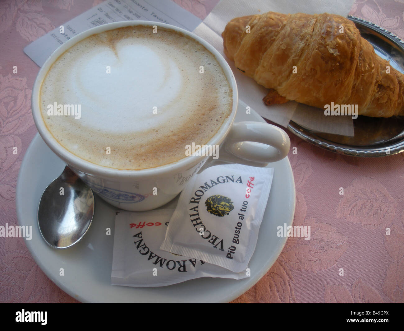 Cappuccino und Croissant serviert auf rosa Tischdecke in Rom, Italien Stockfoto