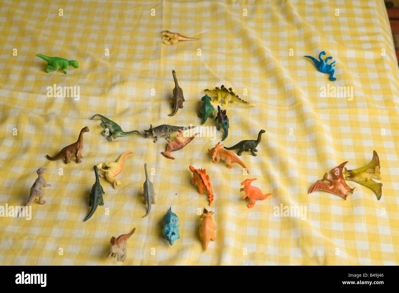 Bunte Reihe von billigen Kunststoff-Spielzeug Dinosaurier liegen verstreut auf karierten gelben und weißen Tuch nach einer Schlacht der Titanen Stockfoto