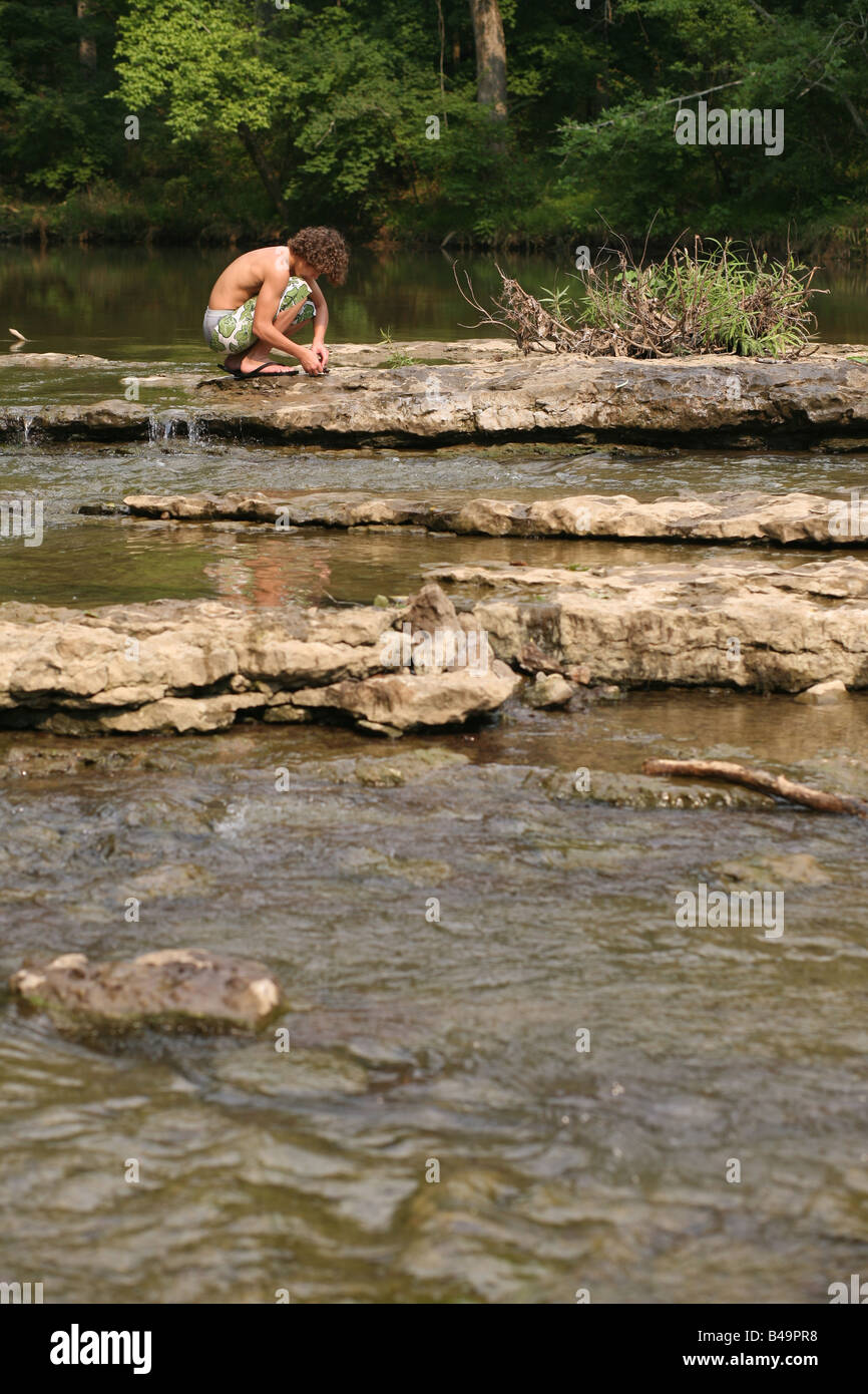 Ein kleiner Junge kniet auf einem Felsen in der Mitte der Harpeth Flüsschen in Nashville, als er eine ganze Reihe von Stöcken macht und verlässt. Stockfoto