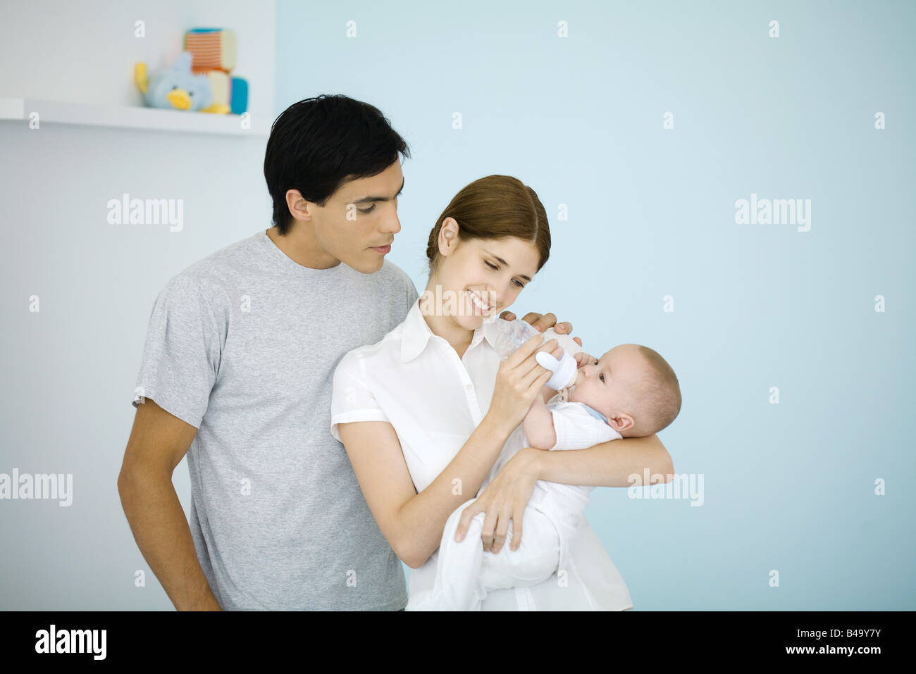 Mutter Fütterung Baby mit einer Flasche, Mann über die Schulter schauen Stockfoto