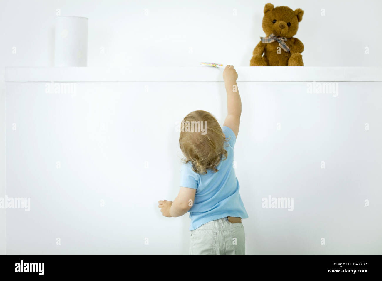 Kleinkind erreichen für Lollipop auf hohen Regal, Rückansicht Stockfoto