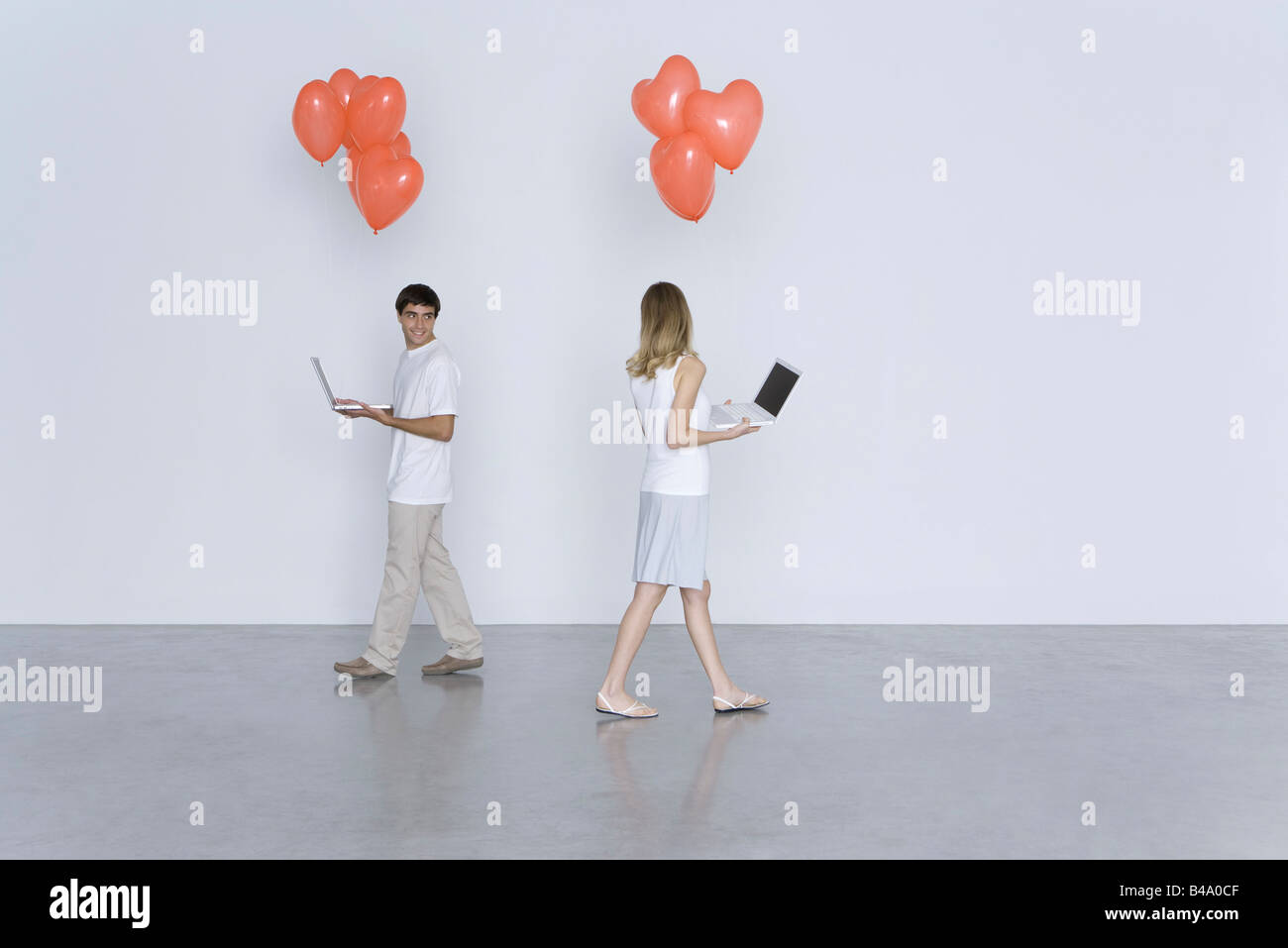 Mann und Frau zu Fuß vorbei an einander, mit Laptops und Herz Luftballons Stockfoto