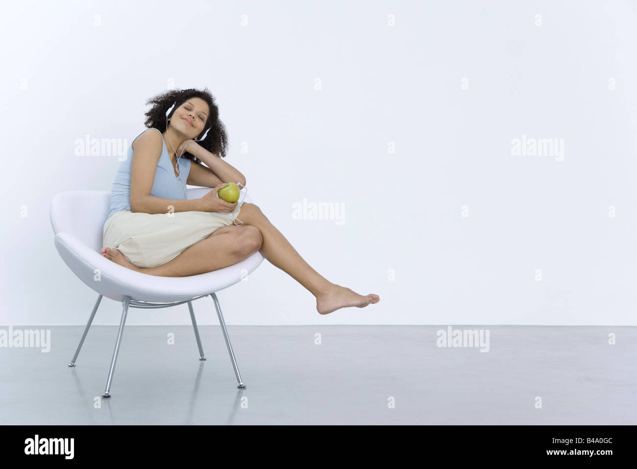 Frau sitzt im Stuhl, hören Kopfhörer angeschlossen an Apple, Lächeln Stockfoto