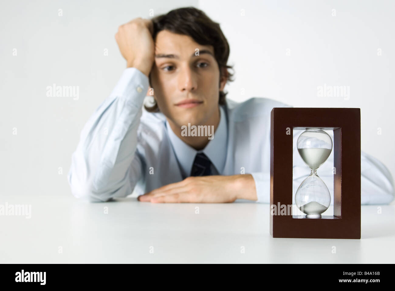 Junger Mann mit Blick auf Sanduhr, Kopf haltend Stockfoto