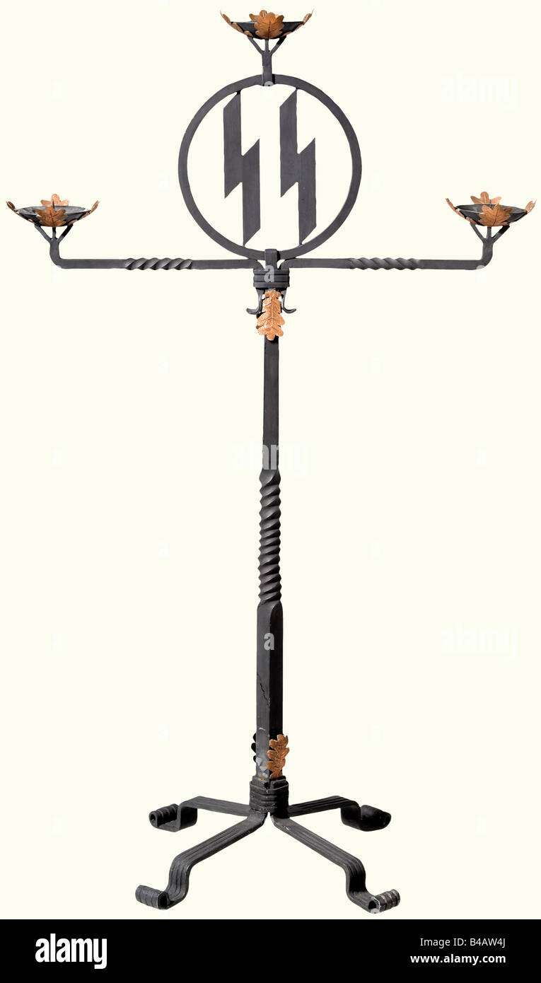 Ein geschmiedetes Eisen SS Hochzeitskandelaber., Geschwärztes Eisen, das mit handgeprägten und gravierten Kupfer-Eichenblättern verziert ist. Drei Kerzenhalter, die Tropfschalen stehen auf "Lebensrunen", und mit öffentem SS-Runen in einem zentralen Medaillon. Kreuzförmige Basis. Höhe 109 cm. Die "Lebensrune" (Algiz rune) ist das Symbol des Lebensborn-Vereins, der 1935 auf Drängen Heinrich Himmlers zur Unterstützung der großen Familien von SS-Angehörigen und der Betreuung bedürftiger Mütter und Kinder von "gutem Blut" in geeigneten Wohnungen gegründet wurde. Der Sitz des Lebensbann, Stockfoto