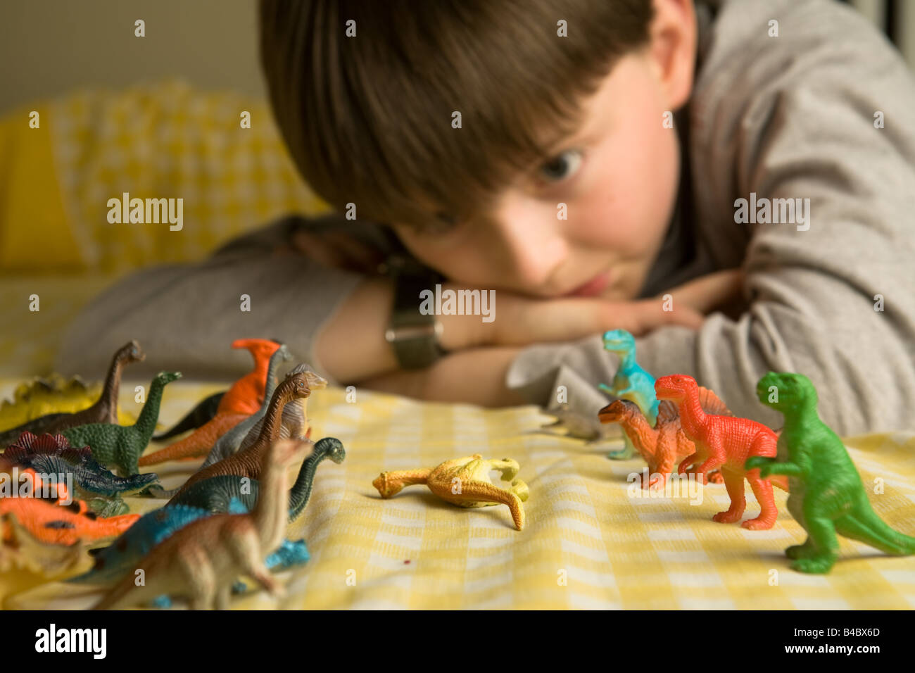 Ein pre-teen junge blickt über eine Horde von bunten Spielzeug Dinosaurier organisiert in Schlacht Reihen mit einem gefällten Diplodocus zwischen Ihnen Stockfoto
