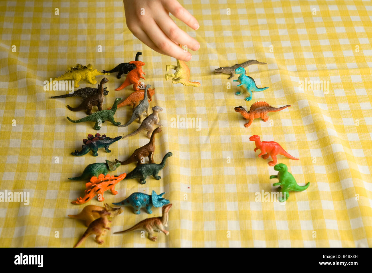 Zwei Reihen der bunten billig Spielzeug Dinosaurier antreten: Fleischfresser und Pflanzenfresser. Eine Kinderhand entfernt einen gefallenen Diplodocus Stockfoto