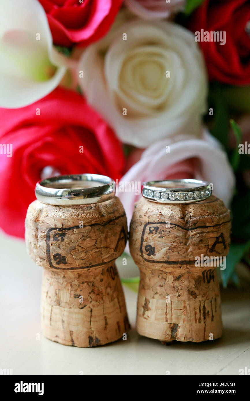 Braut und Bräutigam Trauringe Bands ausgewogen auf Sektkorken mit Brautstrauß Blumen hinter Hochzeit Tag details Stockfoto