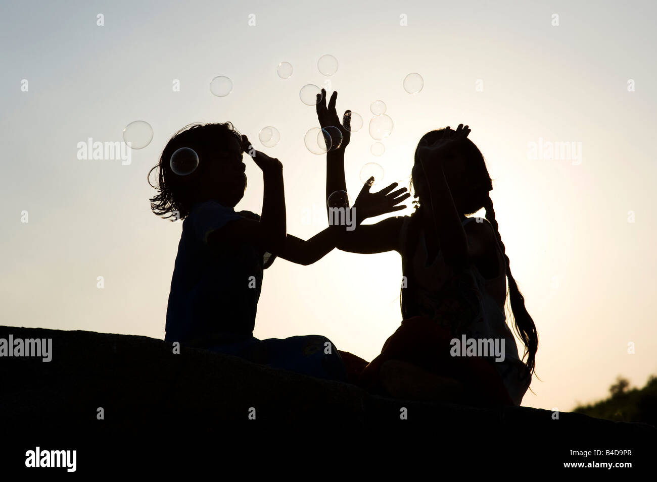 Zwei indische Mädchen sitzt auf einem Felsen spielen mit Luftblasen Silhouette. Indien Stockfoto