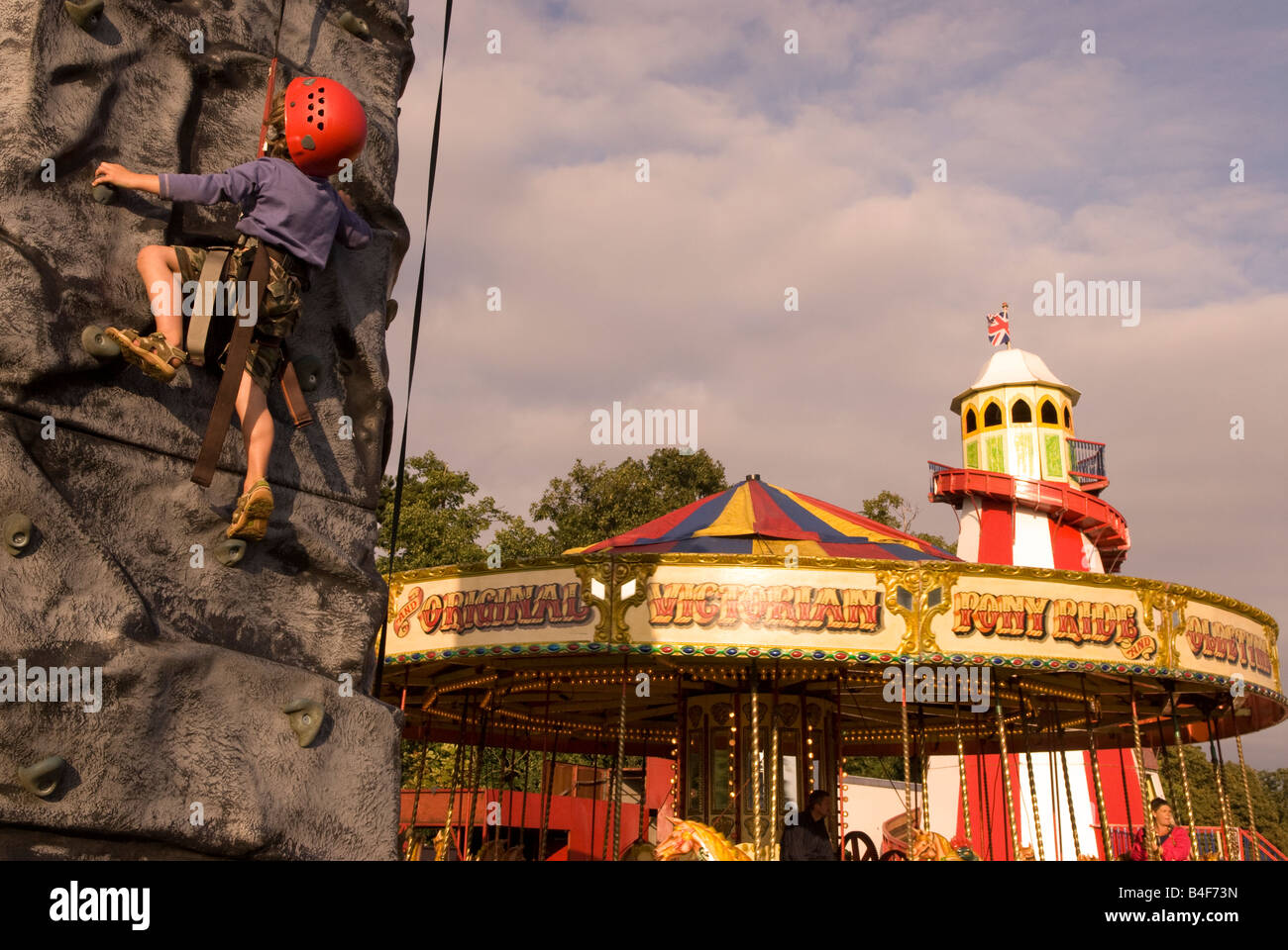 Youngster versucht, Kletterwand mit Messegelände fährt hinter auf Land-Affäre ländlichen Messe, Hampton Court, UK. Stockfoto