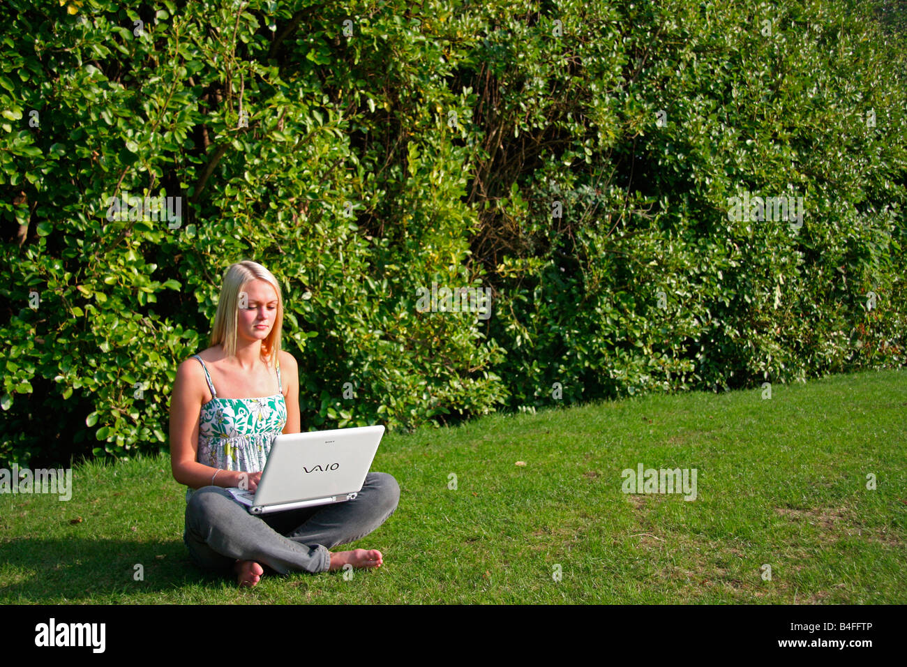 Mädchen sitzen im Schneidersitz auf dem Rasen mit einem laptop Stockfoto