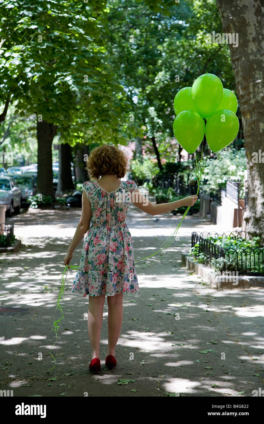 Eine junge Frau zu Fuß eine Stadt Gehweg mit Luftballons, Rückansicht Stockfoto