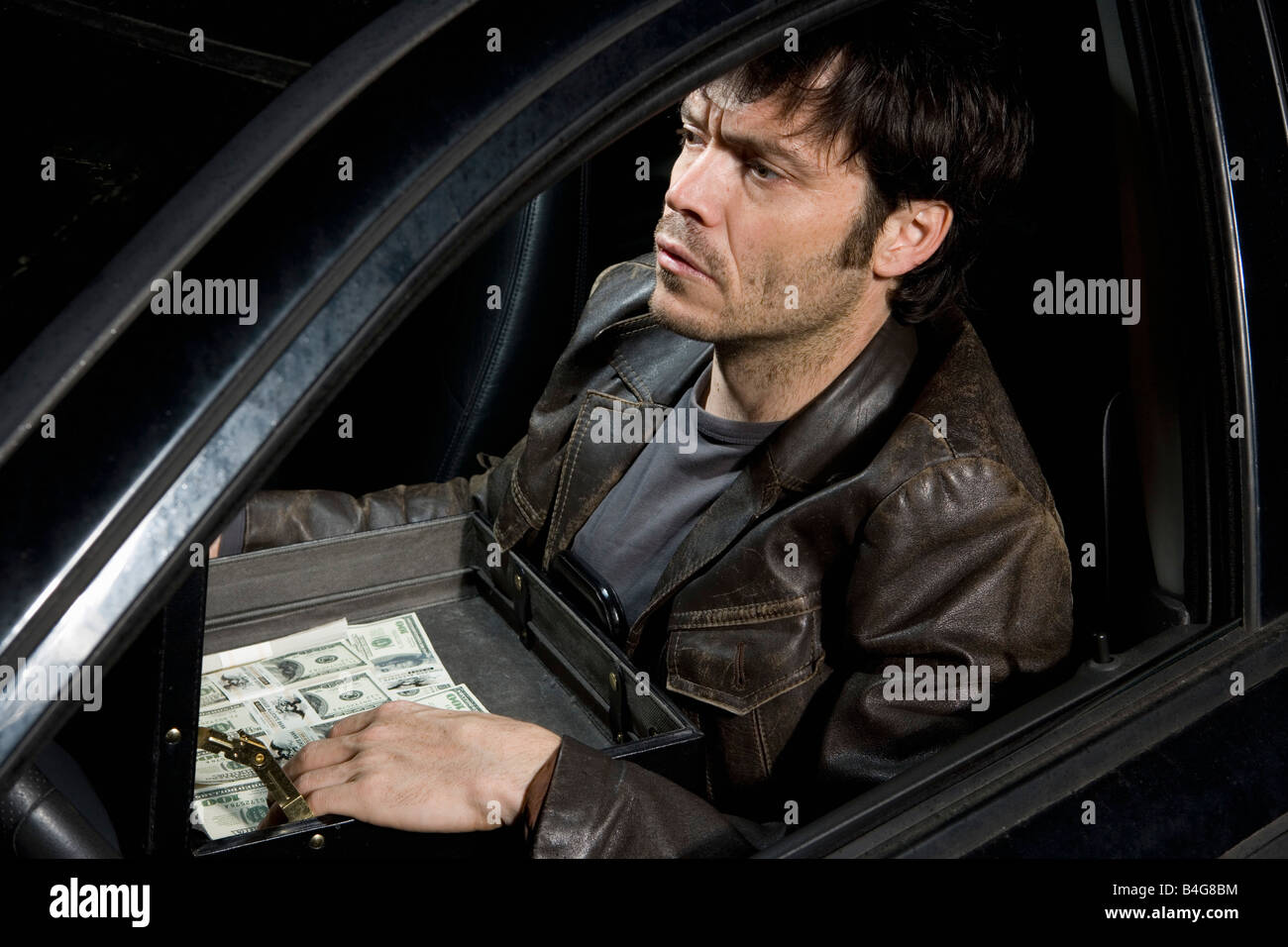 Ein Mann sitzt in einem Auto mit einer offenen Aktentasche voller Geld Stockfoto