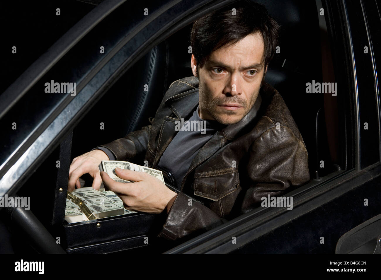 Ein Mann sitzt in einem Auto mit einer offenen Aktentasche voller Geld Stockfoto