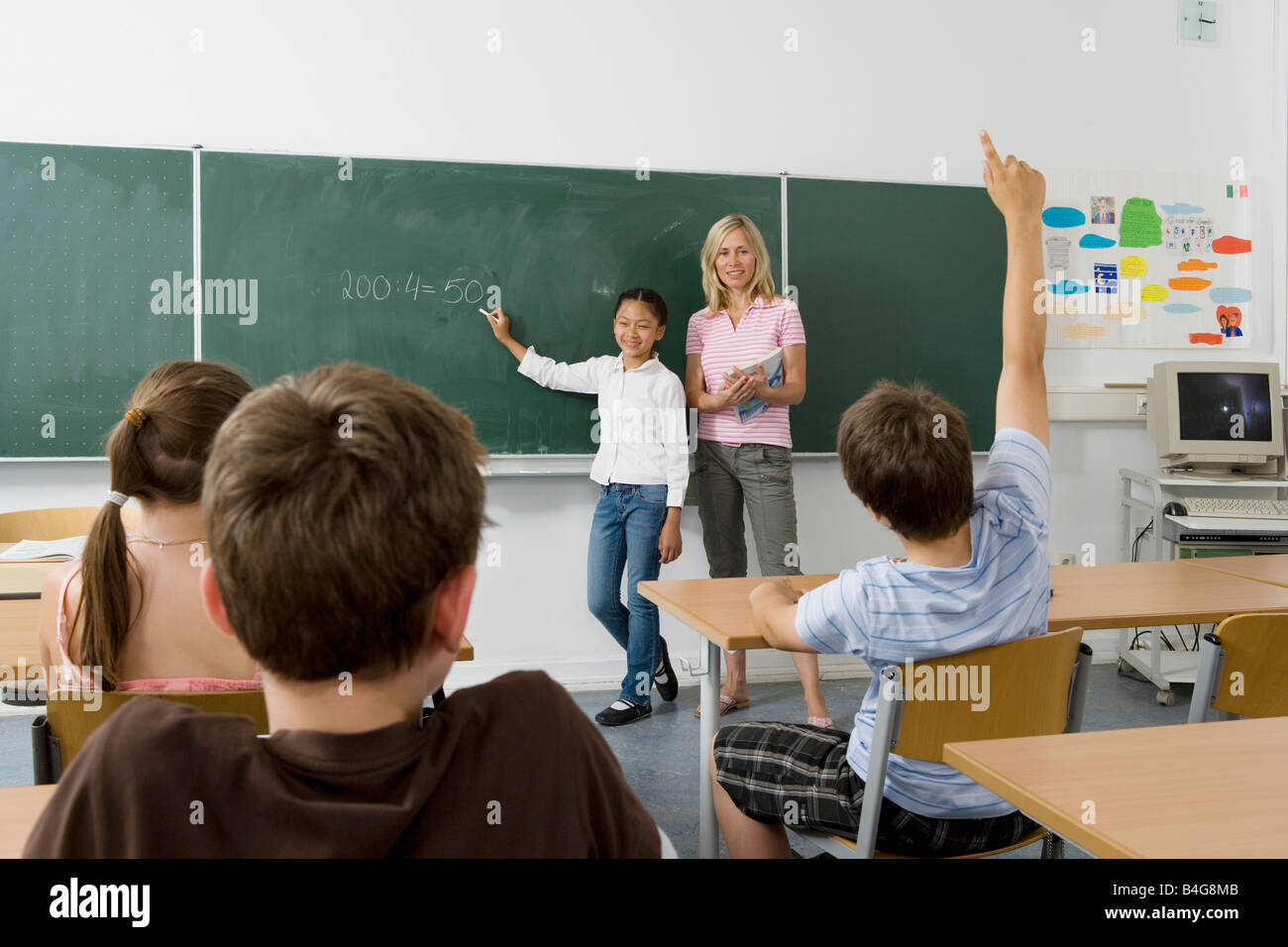Ein Lehrer und ein Schüler an der Tafel, mit Blick auf die Klasse Stockfoto