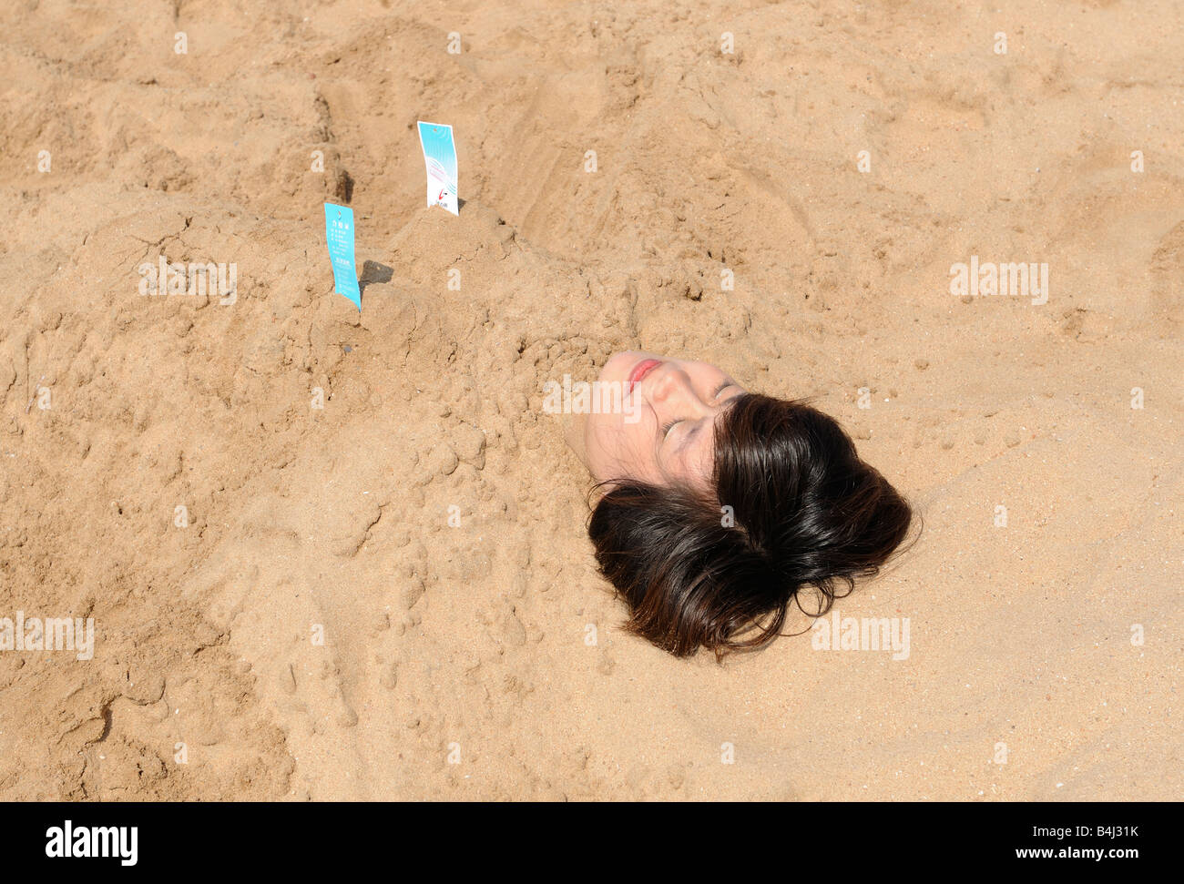 Eine Dame bedeckt im Sand am Strand von Qingdao, Shandong, China.03-Oct-2008 Stockfoto