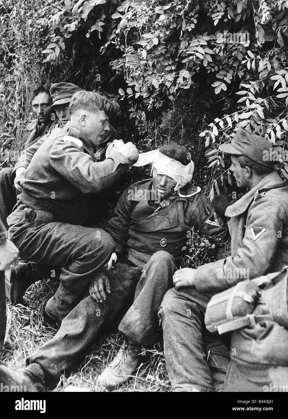 Britische Armee Sanitäter neigt dazu, einen verwundeten deutschen Gefangenen nach seiner Gefangennahme im französischen Dorf Lingevres während dem 2. Weltkrieg 1944 Stockfoto