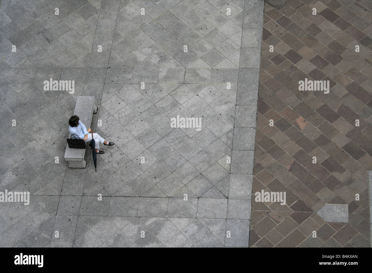 Alleinerziehende Frau, die auf einer Bank auf einem öffentlichen Platz sitzt. Blick von oben. Stockfoto