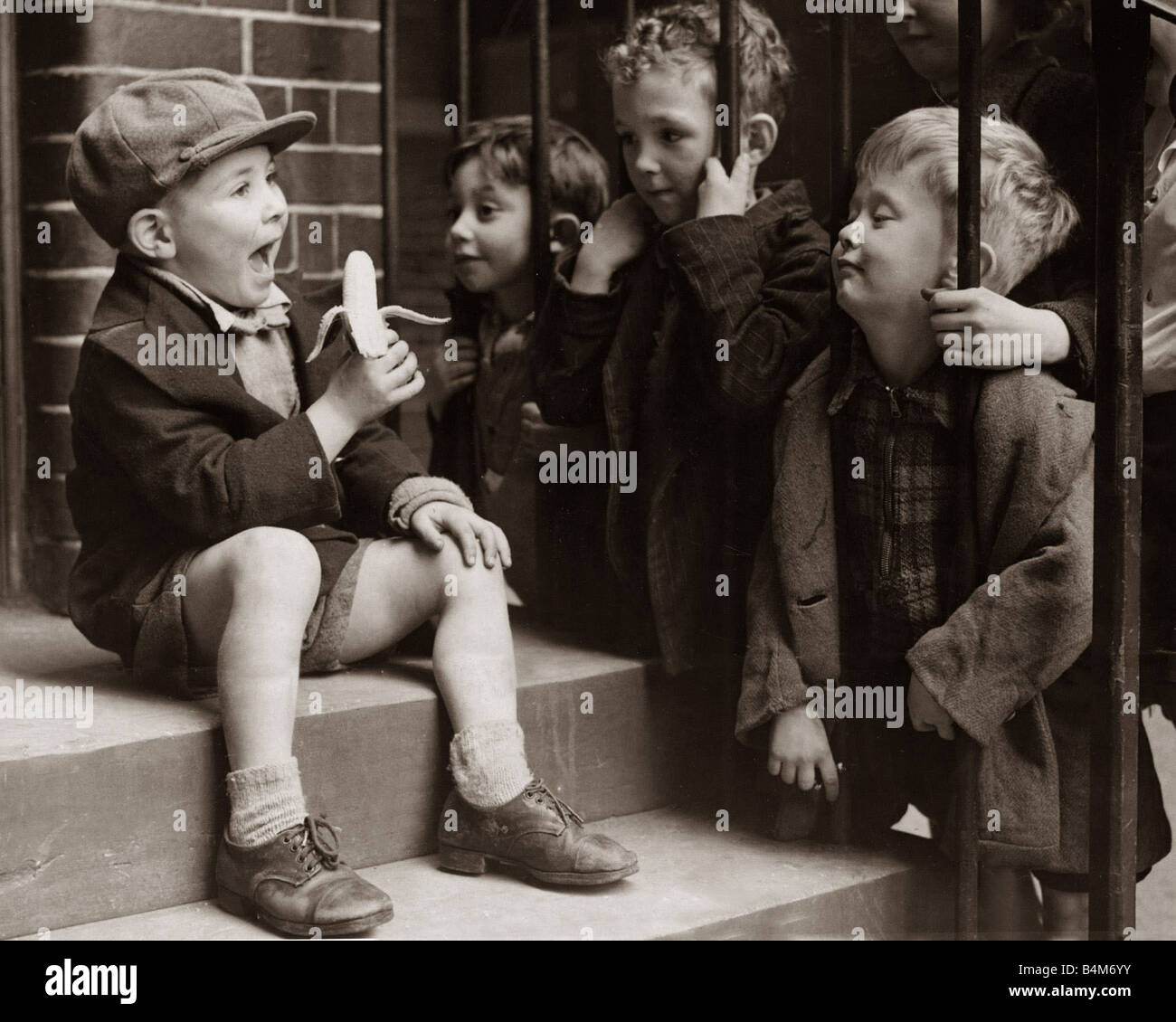 Ein kleiner Junge hält eine Banane, während andere Kinder sehnsüchtig sie in der Hoffnung bestaunen, ein Stück von der verbotenen Frucht durch Metallgeländer versuchen lassen Sie mich Ihnen sagen, dies ist kein gewöhnliches Banane Oktober 1942 Stockfoto