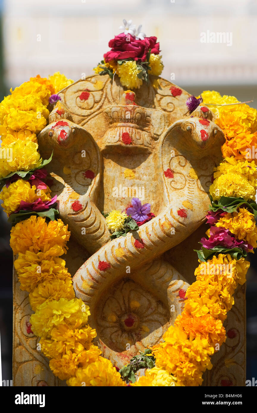 Naga. Indische Kobra Gottheit Steingötzen bedeckt Blumengirlanden für hindu Puja-Zeremonie. Puttaparthi, Andhra Pradesh, Indien Stockfoto