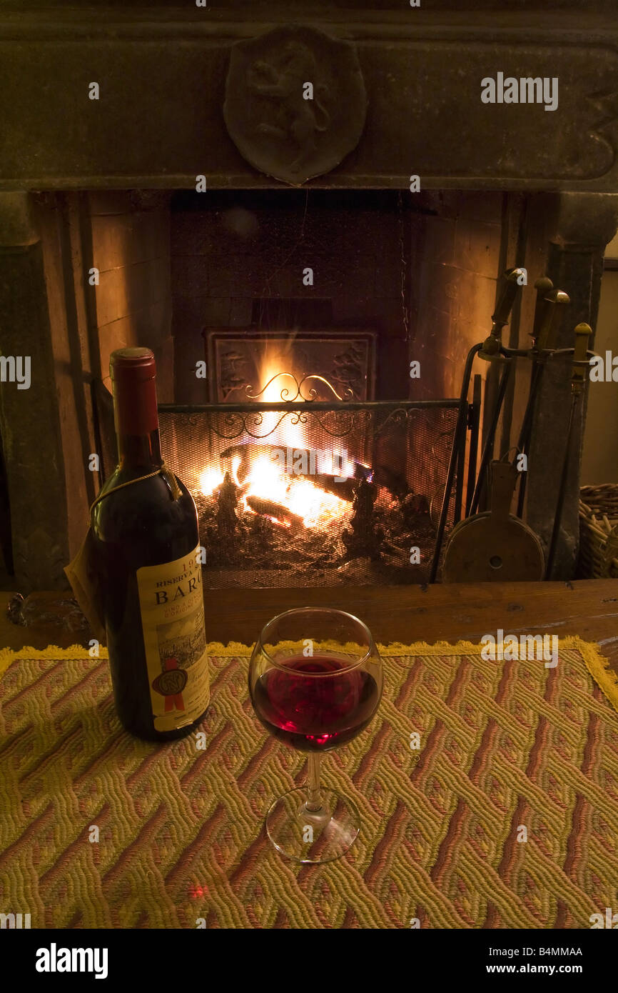 Glas Rotwein und eine Flasche auf einem Holztisch vor einem Kamin aus Stein Stockfoto