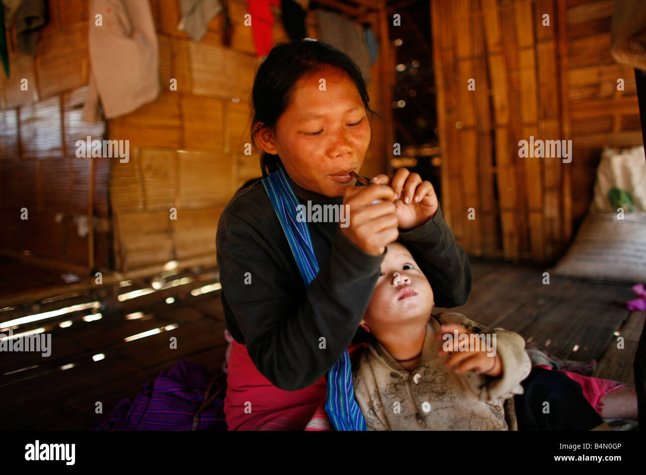 Eine burmesische Mutter Lichter ihr Rohr in ihrer Hütte, während ihr Baby In Myanmar Birma Tausende von Menschen Uhren haben in der Nähe von der Grenze als Folge der Unterdrückung in ihrem Heimatland um 200 birmanischen Vertriebenen, in La niedergelassen haben pro Her ein Dorf auf der burmesische Seite der Grenze zu Thailand in der Nähe der thailändischen Stadt von Mae Sot sie ablehnen, weil sie wollen, in ihrer Heimat bleiben diese Flüchtlinge über die Grenze angesiedelt unterstützen die Rebellen Bewegung mit dem Namen Straflosigkeit Karen National Liberation Army betreibt in östlichen Birma Jan 2007 Stockfoto