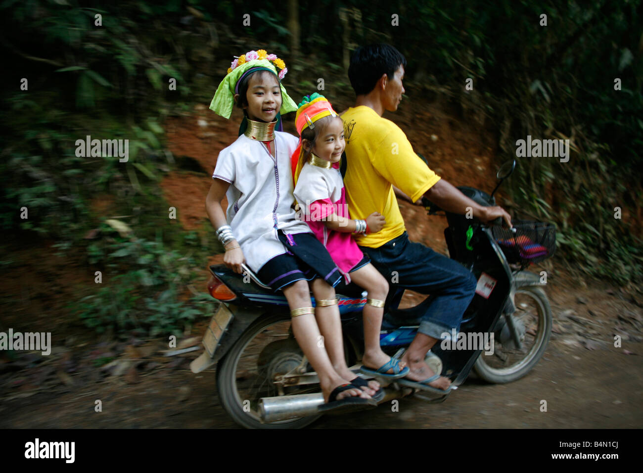 Longneck Familienangehörigen fahren auf einem Moped etwa 300 birmanischen Flüchtlinge in Thailand Mitglieder der indigenen Gruppe bekannt sind als die Longnecks, die größte der drei Dörfer wo live Longnecks Nai Soi genannt befindet sich in der Nähe von Mae Hong Son Stadt longnecks, Metall tragen Ringe auf den Hals, die das Schlüsselbein nach unten drücken und verlängern dem Hals, sie sind, eine touristische Attraktion Touristen besuchen Nai Soi zu fotografieren die Longnecks und ihr Kunsthandwerk kaufen Die Dörfer sind als menschliche Zoos von Menschenrechtsorganisationen kritisiert. Stockfoto