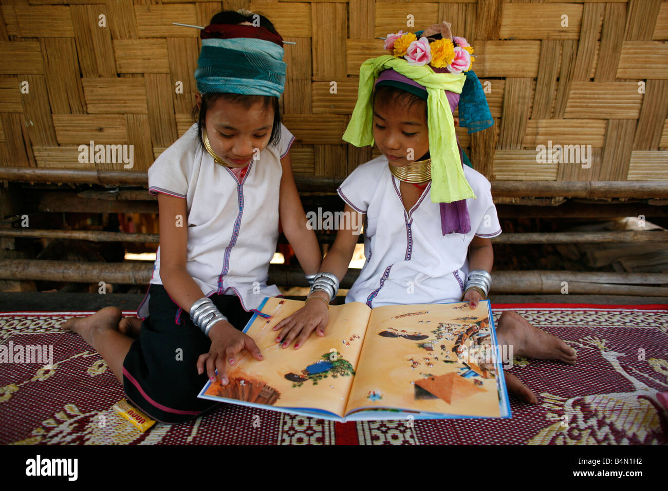 Zwei junge Longneck Mädchen betrachten ein Buch zusammen etwa 300 birmanischen Flüchtlinge in Thailand Mitglieder der indigenen Gruppe bekannt sind als die Longnecks, die größte der drei Dörfer wo live Longnecks Nai Soi genannt befindet sich in der Nähe von Mae Hong Son Stadt longnecks, tragen Metallringe auf den Hals, die das Schlüsselbein nach unten drücken und verlängern dem Hals, sie sind, ein Tourist Anziehung Touristen besuchen Nai Soi zu fotografieren die Longnecks und ihr Kunsthandwerk kaufen Die Dörfer sind als menschliche Zoos von Menschenrechtsorganisationen kritisiert. Stockfoto