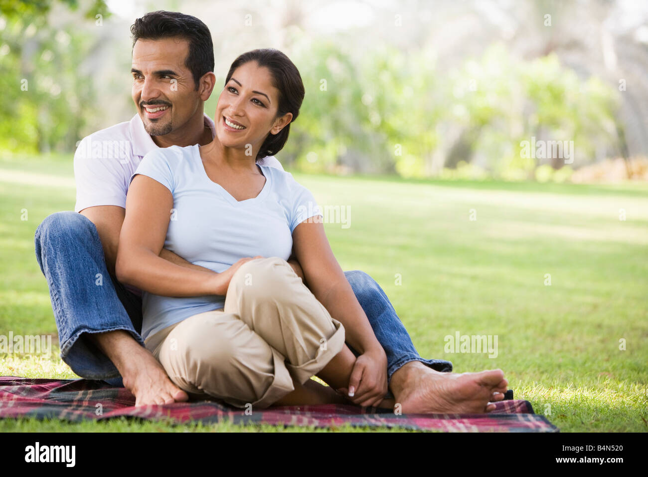 Paar sitzt draußen im Park lächelnd (Tiefenschärfe) Stockfoto