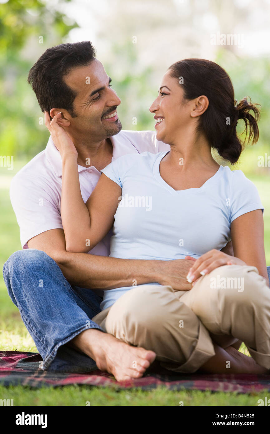 Paar sitzt draußen im Park ist anhänglich und lächelnd (Tiefenschärfe) Stockfoto
