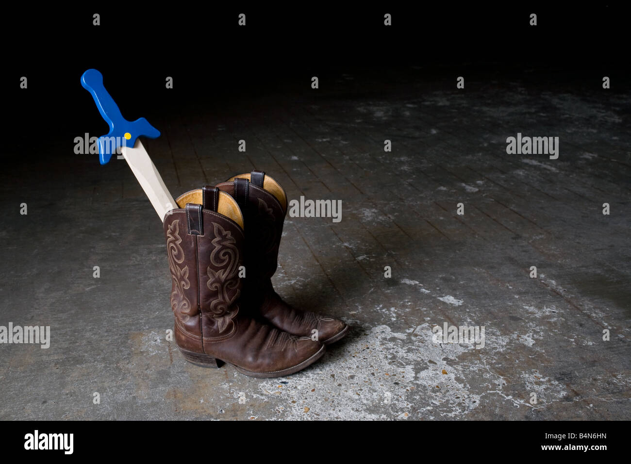 Ein paar getragene Cowboy Stiefel mit einem Kind Spielzeug Schwert ragt, als Symbol der Erwachsene Vorbild für Kinder und emulation Stockfoto