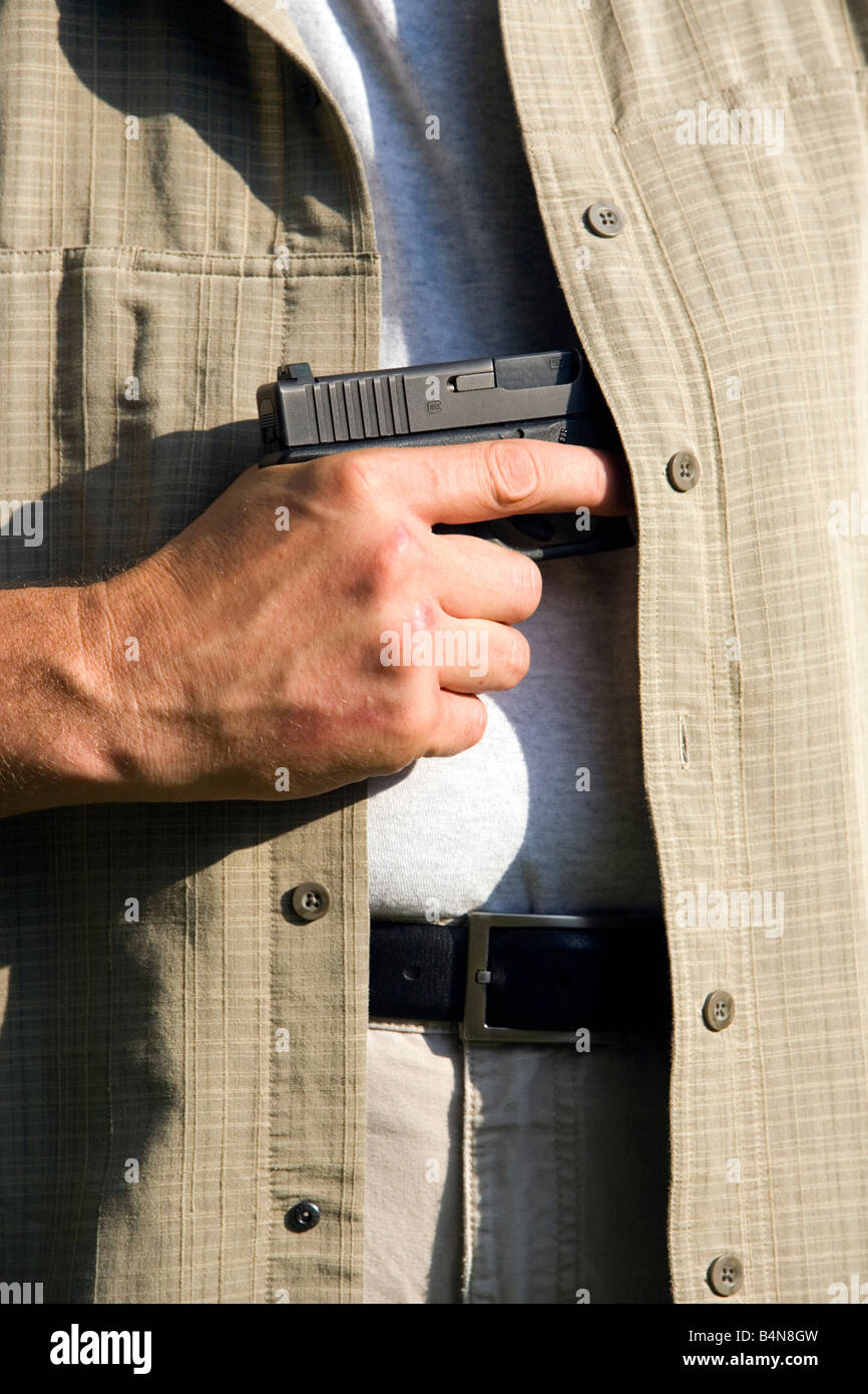 Ein Mann zieht eine verborgene Pistole Waffe aus seinem Hemd. Stockfoto