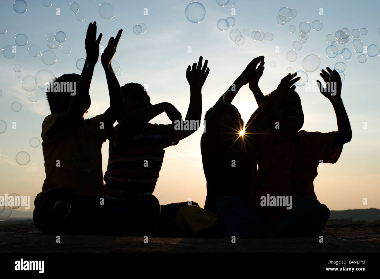 Vier indischen Jungen sitzen auf einem Felsen spielen mit Luftblasen Silhouette. Indien Stockfoto