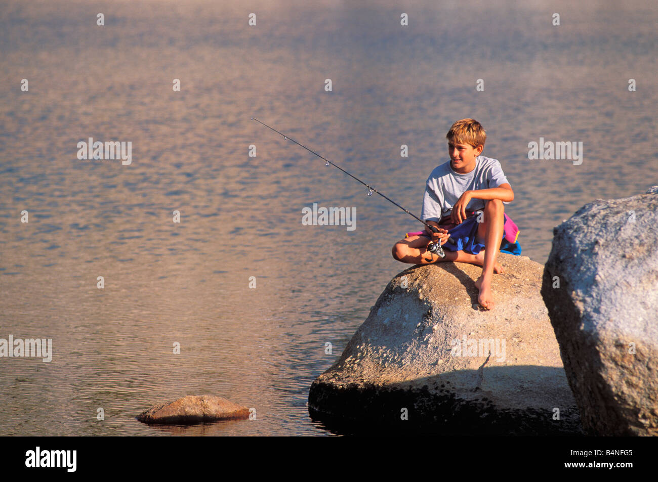 Junge, Fischen von einem Felsen am Ufer von Budd Lake Tuolumne Meadows Bereich Yosemite National Park in Kalifornien Stockfoto