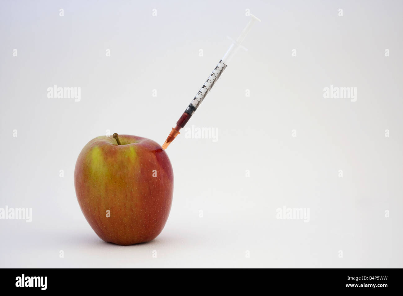 Apfel mit Spritze mit roter Flüssigkeit hinein auf einem weißen Hintergrund kleben Stockfoto