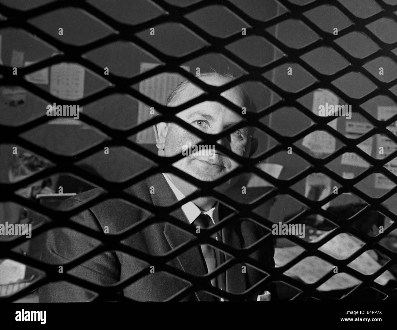 Buchmacher Sidney Glanz im Bild durch die Gitteröffnungen im Inneren seine Wettbüro in der Isle Of Man kein Bargeld Wetten darf in seinem Geschäft Juni 1969 Stockfoto