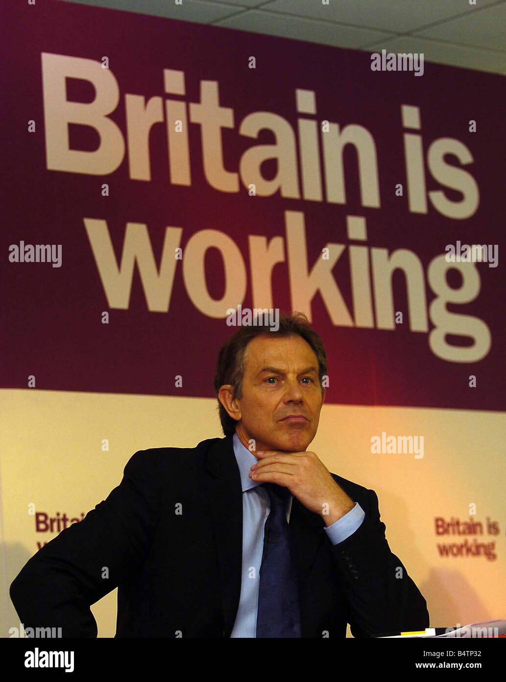 Premierminister Tony Blair in Leeds zur Förderung der lokalen Wahlkampagne sitzen vor Motto Großbritannien arbeitet Parolen, die Kampagnen, die den Hals berühren Kinn mit der Hand schieben Lippen vorausschauendes Denken Ausdruck nachdenklichen Ausdruck kritischen vorsichtig Mai 2004 Stockfoto