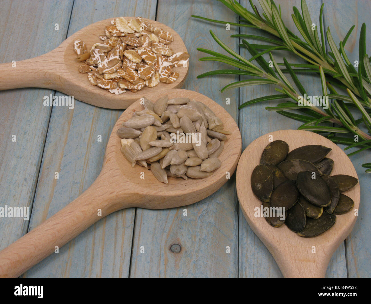 drei Arten von Samen auf Kochen, Löffel und eine Handvoll Rosmarin auf einem Holztisch Stockfoto